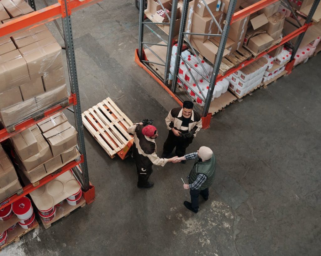 2 Leute in einem Logistikzentrum die sich einen Handschlag geben. Hoffentlich für einen Feinverteilungsdeal.